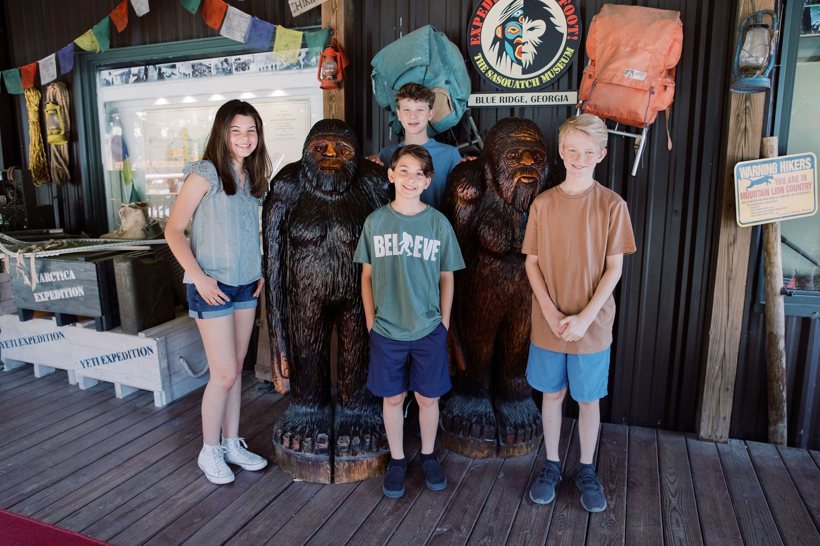 children standing next to carved statues of Bigfoot